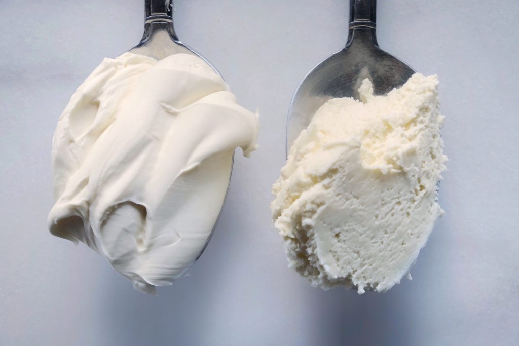One spoon of smooth mascarpone cheese next to another spoon of curdled mascarpone cheese
