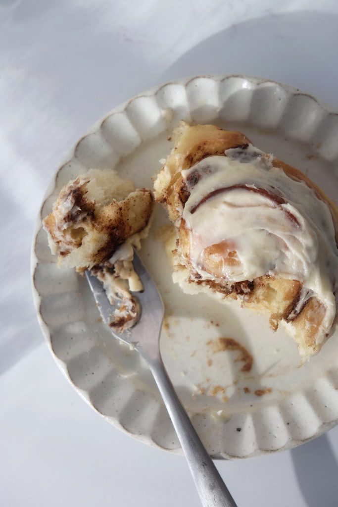 Cinnamon roll topped with cream cheese frosting on a plate