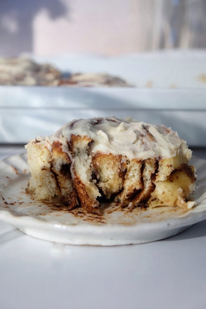Cinnamon roll topped with cream cheese frosting on a plate, cut in half to reveal cross-section