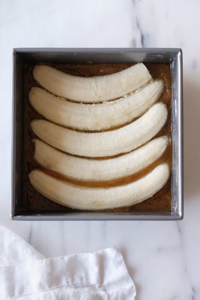 Square baking pan with bananas placed over melted butter and brown sugar mixture