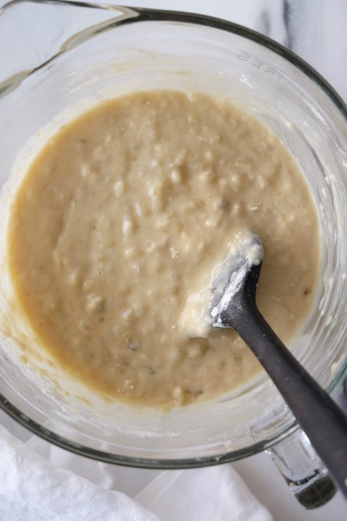 Glass bowl with caramelized banana upside down cake batter; dry ingredients folded with rubber spatula
