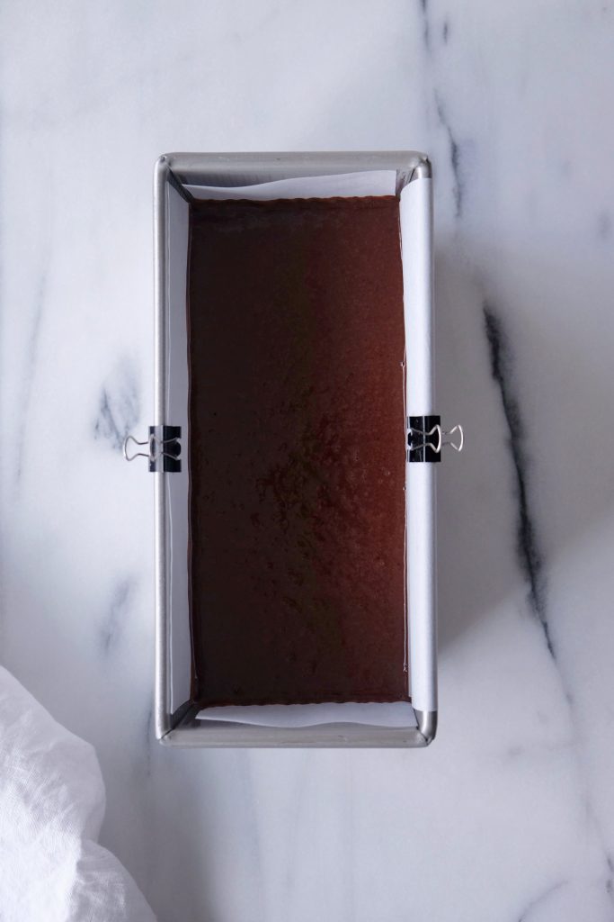 Loaf pan lined with parchment paper, with chocolate cake batter