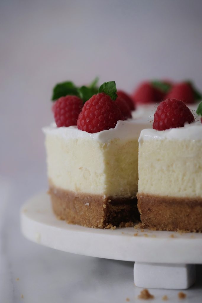 New York cheesecake with sour cream topping, garnished with raspberries and mint leaves