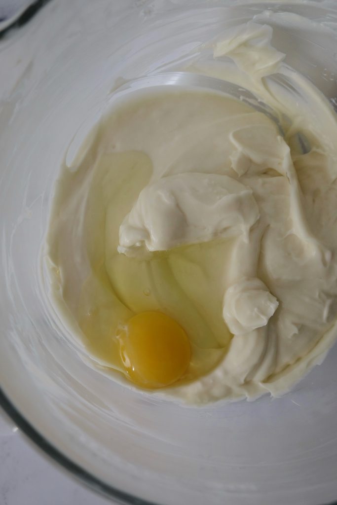 Glass bowl with cheesecake batter and one egg