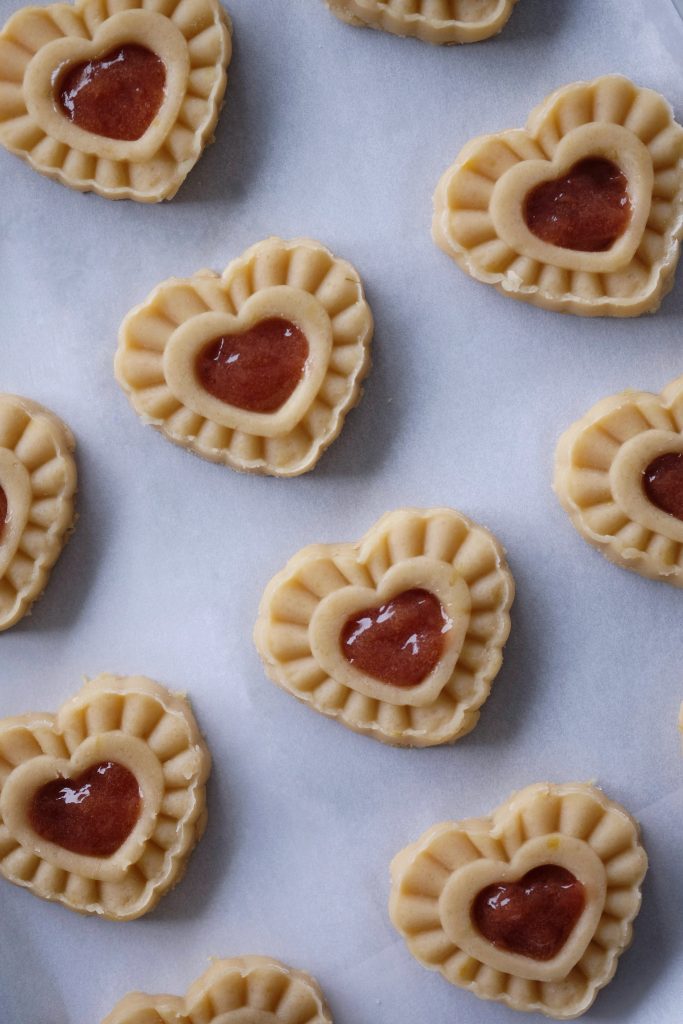 Strawberry lemon heart thumbprint cookie dough on a baking pan, with their jam filling