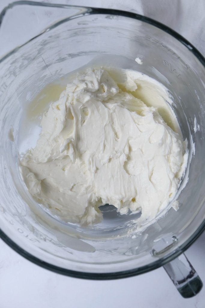 Glass bowl with cream cheese and sugar beaten with a hand mixer