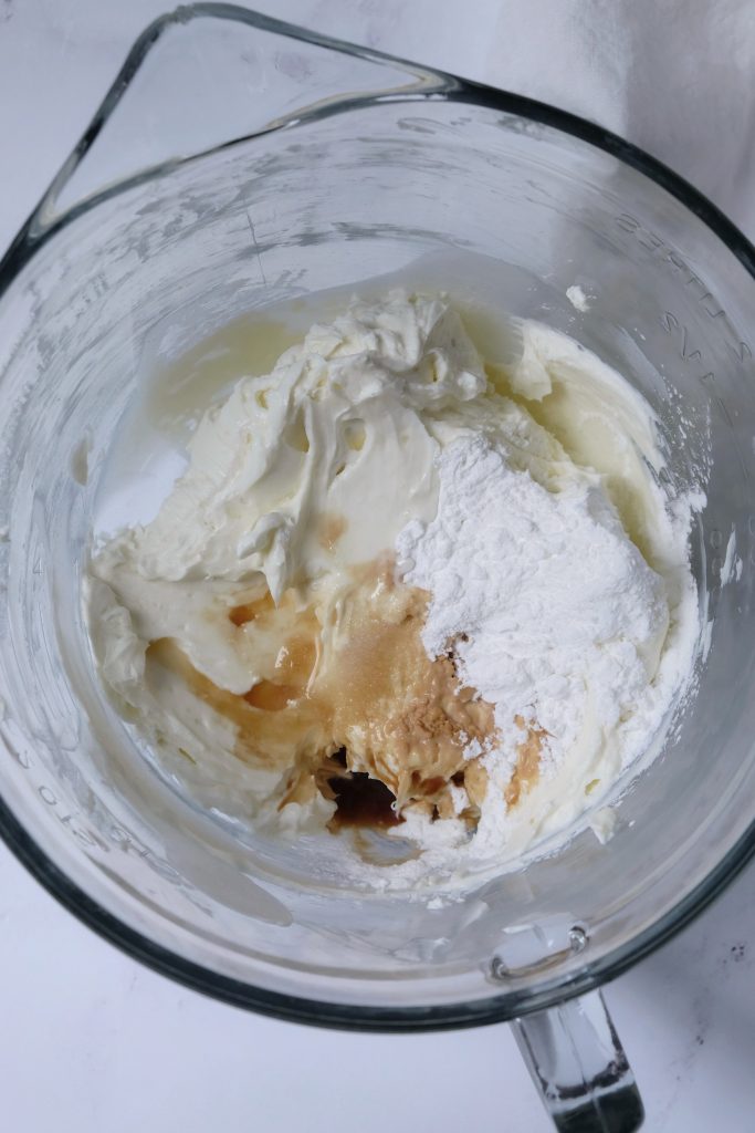 Glass bowl with beaten cream cheese and sugar, with cornstarch, salt, vanilla extract, and lemon juice just poured over