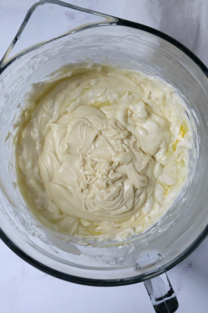 Cheesecake batter in a glass mixing bowl, with melted white chocolate just poured over