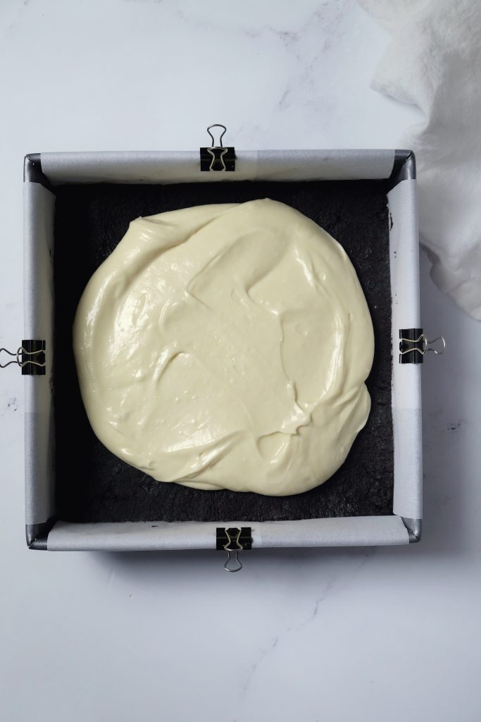 Square baking pan with chocolate cookie crust and cheesecake batter