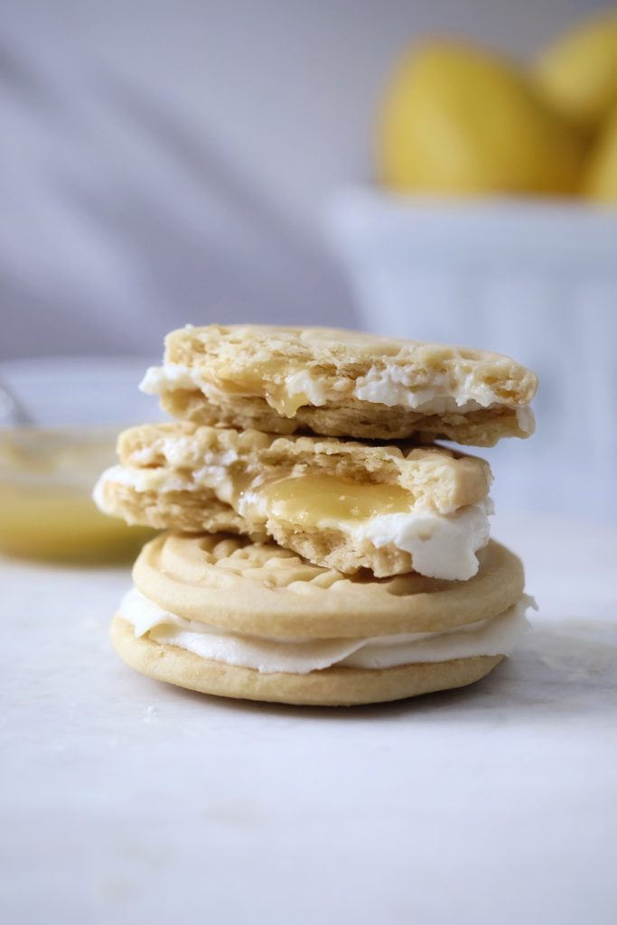 Stack of lemon cheesecake sandwich cookies, cut in half to reveal cross-section